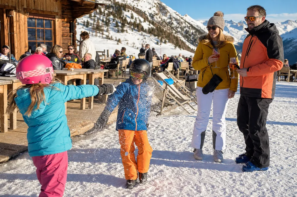 Kinderen met skihelm spelen in de sneeuw bij een berghut