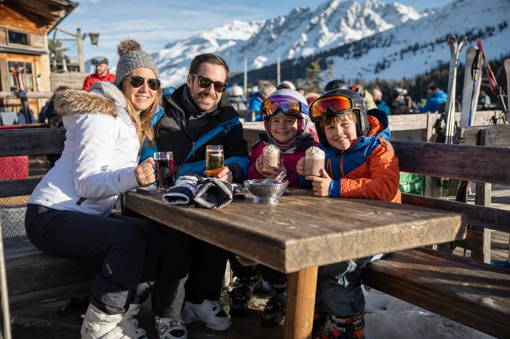 Gezin met warme chocolademelk op een zonnig terras aan de piste